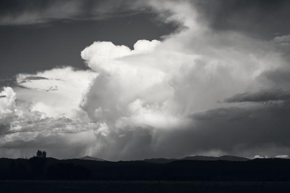 Large, dramatic clouds loom over a distant mountain range in a grayscale landscape.