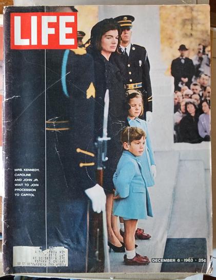LIFE magazine cover from December 6 1963
Photo caption reads "Mrs. Kennedy, Caroline and John Jr wait to join procession to Capitol"
The Kennedys stand on some steps, surrounded by two soldiers. In the background (out of focus) a crowd of people watch them.