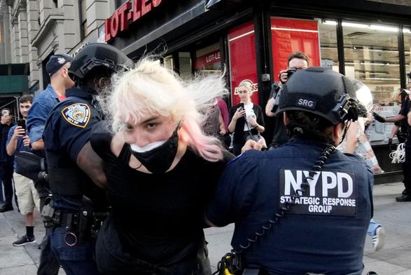 A young blond woman with a face mask is being detained by two police.