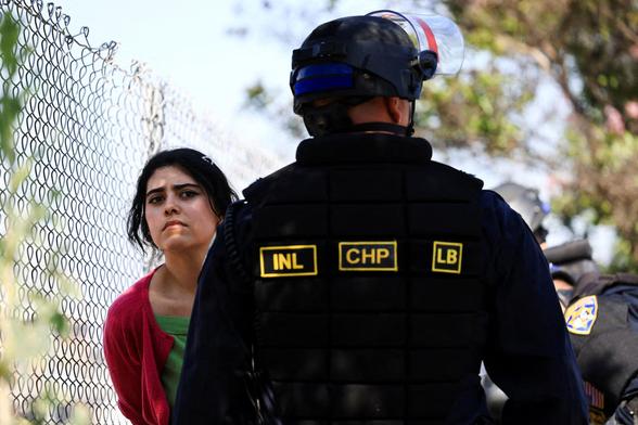 A young woman dressed in green & red is being detained.
