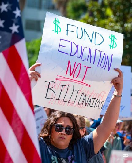 A woman holding a sign that says, "fund education, not billionaires."