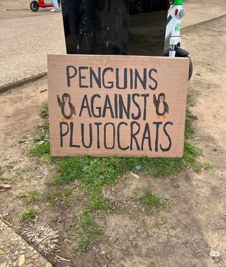 A cardboard sign with two penguins with their fists in the air that says, "Penguins against Plutocrats!"