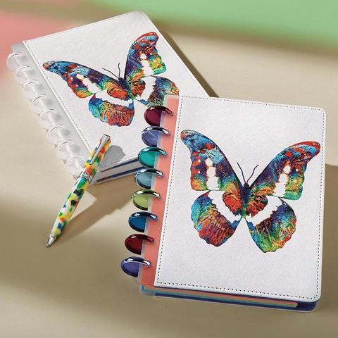 White notebooks with colorful butterfly art by Sharon Cummings.