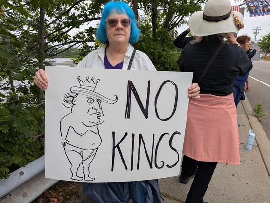 a woman holds a sign with the words "No Kings Day," beside a caricature of Donald Trump wearing only white briefs and a crown.