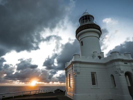 A lighthouse with the sea and the rising sun behind it