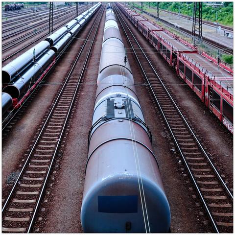 Three long lines of freight cars carrying pipes, tanks, and empty autoracks, respectively, vanishing in the distance.
