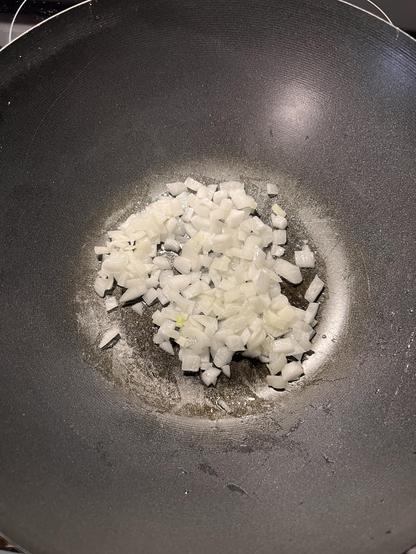 A photo looking into the bottom of a wok at diced onions cooking in oil.