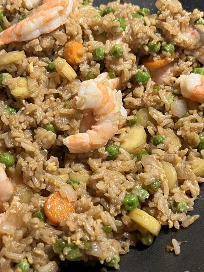 Photo of a wok full of fried rice, with cooked shrimp, peas, bits of carrot and onion visible.