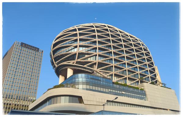 An office building formed like an egg in top of some square structure.