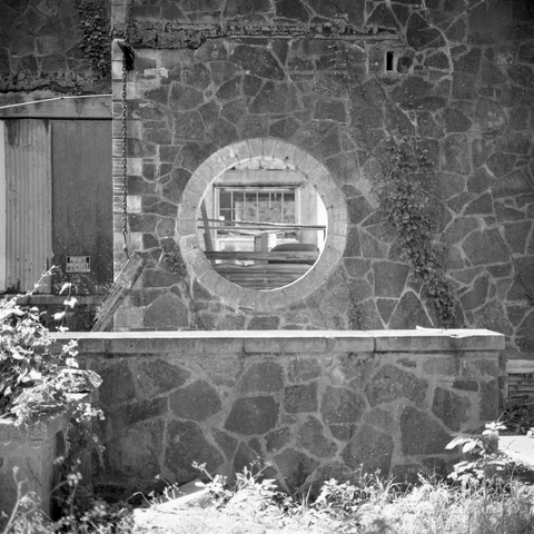 A black and white film photo. A circular window at an abandoned building reveals its weatherworn interior in San Gabriel, Texas. Sunday, June 15, 2025.