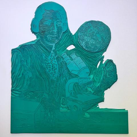 Photo of my carved Lino block portrait (on green vinyl, against a white background) of neuroscientist Rita Levi-Montalcini in 1940, at a desk with compound binocular microscope, leaning on an incubator, holding an egg and looking at the viewer. Behind her is a large circular image of a photograph of nerve cells she took with this microscope.