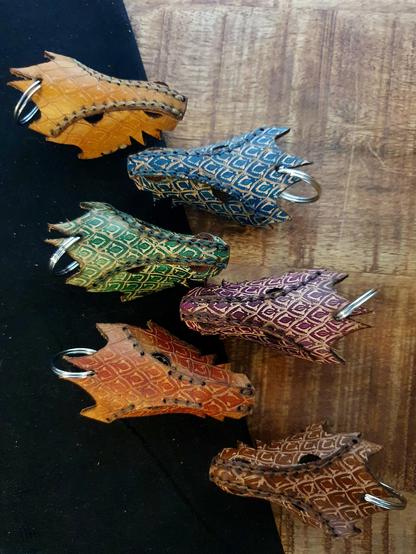 6 Leather dragon keychains in front of a black and wood background