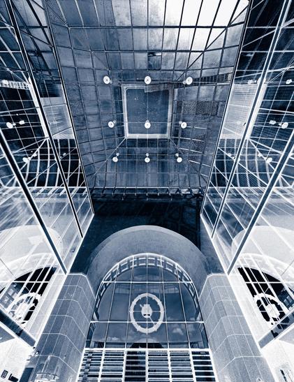 A blue-tinted monochrome image of the interior of the Mannheim main station, showing lots of glass and steel, with the station clock at the bottom. The intensities have been inverted.