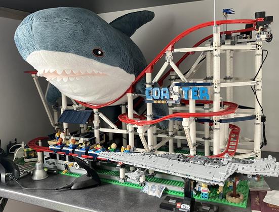 A big Blåhaj cuddly shark sitting on top of a Lego model of a roller coaster.