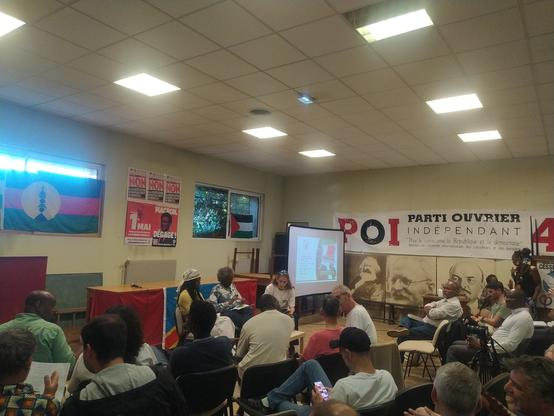 Photo de la salle, au mur le drapeau kanak, plusieurs affiches de propagande et une banderole POI (parti ouvrier indépendant)
