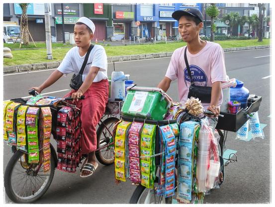 Two hawkers on bicycles, selling drinks.