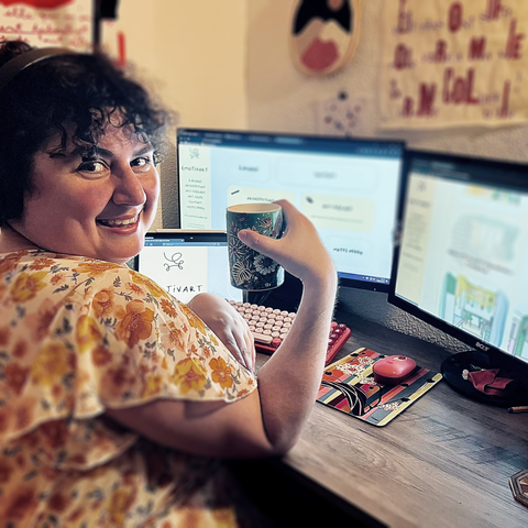 Une photo pas du tout naturelle de moi, je tiens une tasse dans la main.
Dans le fond on voit mes trois écrans avec le site (mon site) emotivart.fr dessus.