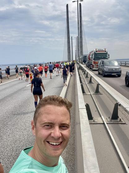 Person taking a selfie on the Øresund bridge, one side full of runners, the other side filled with cars stuck in traffic