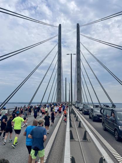 On one side runners on the Øresund bridge, on the other side cars stuck in traffic. Despite the traffic people in the cars are motivating the runners.