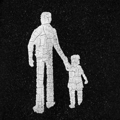 A photo of a pedestrian sign painted on pavement showing a weathered white silhouette of a man holding a child's hand on a black asphalt surface.