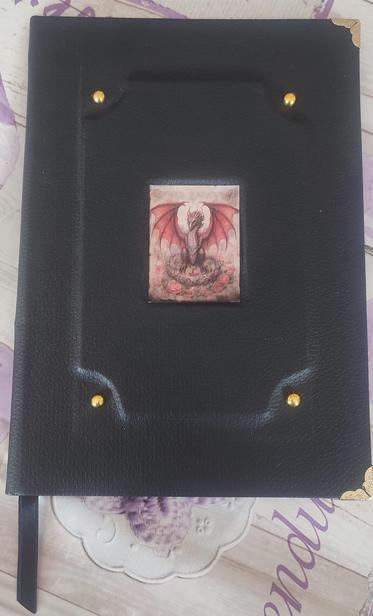 Hardcover booklet with black faux leather cover. An embossed frame with rounded corner (inward) and decorative rivets on the four corners. In the center there is a a red dragon sticker. 
On the corners there are book corner protectors