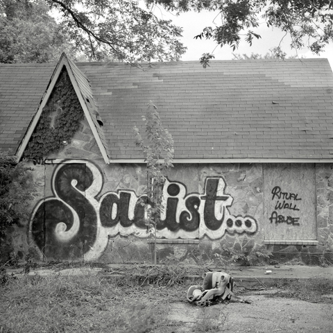 A black and white film photo. An abandoned house has a large graffiti tag that reads “Sadist… Ritual Wall Abuse” in Austin, Texas. Monday, June 23, 2025.