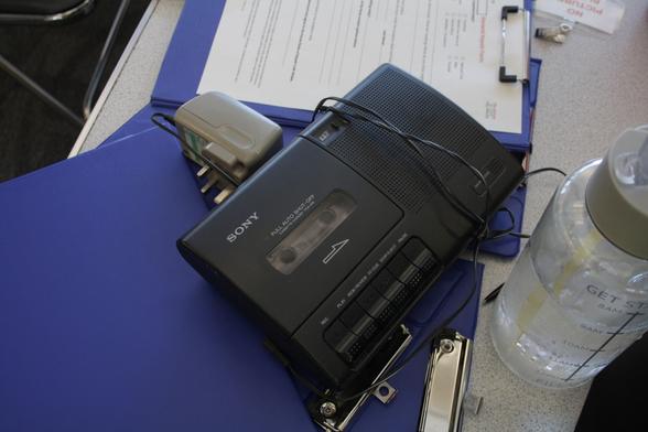 A black sony tape player with the cable wrapped around it laying on a blue clipboard.