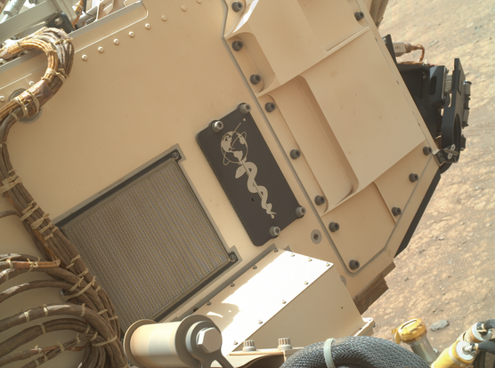 A special aluminum plate on the rover's left side bears an image of planet Earth supported by the Rod of Asclepius, an ancient Greek symbol displaying a snake-entwined rod to symbolize healing and medicine.