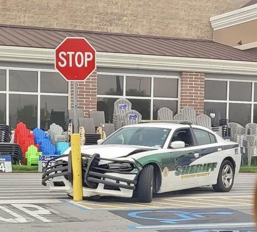 A sheriff has run amiss in a parking lot, slamming the front of their car into a bollard with a stop sign.    The crash bar is bent, the hood is popped.... considerable frontend damage!