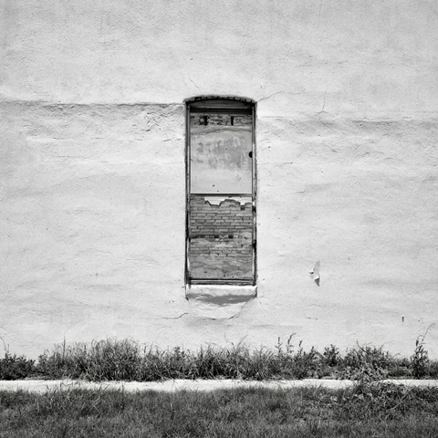 A black and white film photo. A narrow window on the side of an old abandoned building reveals the interior brick wall in Bartlett, Texas. Sunday, June 15, 2025.