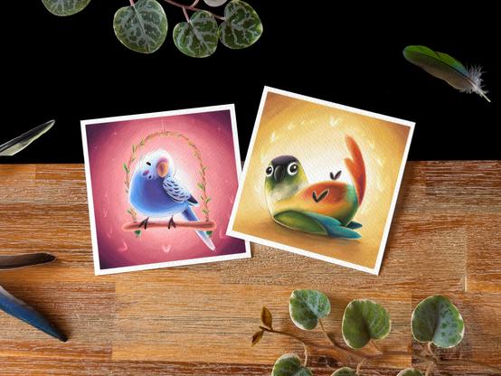 Picture of two small square print on a black and wooden background; a few conure and budgie feathers decorate the backdrop as well as a few little plants. 
The print on the left is of a little blue budgie happily sitting in a swing, and the print on the right is of a little green cheek conure leaning playfully on its back.