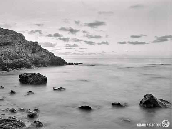 A black and white long exposure photograph looking out to sea at sunrise.