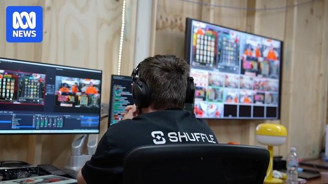 Someone sitting in front of a bank of computer screens, their shirt says "Shuffle" on the back