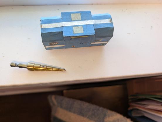 Old concept model I built in 1979 for a boxcar to be used on a lunar railroad. It is cardstock and 1/48th scale. It is light blue, with various stripes and small decals, boxy, short, and low to the ground. There are two sets of wheels, but they aren't visible in the photo. The sides of the roof are beveled, except for a plain-box center section with double pressure loading doors on each side. 
    This is the top view of the model, more clearly showing the roof shape and the boxy center area for loading and unloading of the ends and to hold bulkier items.