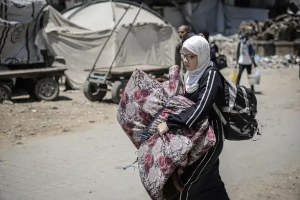 A young woman in glasses flees, carrying nothing but a folded mattress and a small backpack.