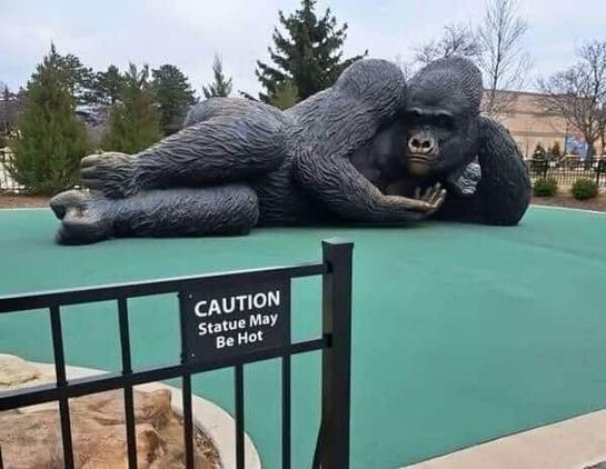 mini golf hole, with a giant statue of a gorilla laying in a sexy pose and a sign that says: caution statue may be hot