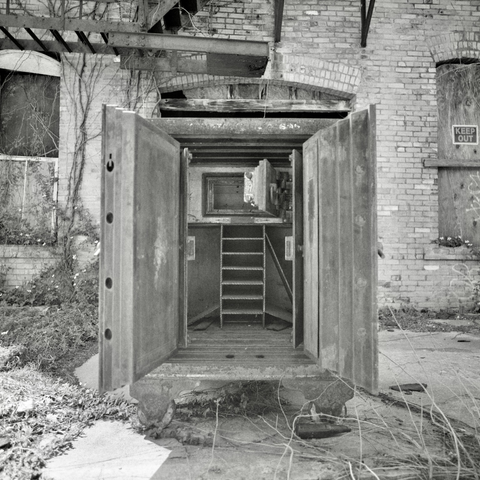 A black and white film photo. A large antique metal safe sits open outside an abandoned building in Smithville, Texas. Saturday, March 22, 2025.