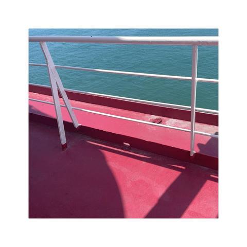 locking at a white ship's railing casting its shadows on the red painted deck. the shadows create interesting shapes. in the background the blue ocean completes this summer color palette