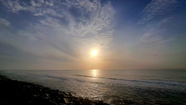 Morning sunrise over the Bay of bengal. Sky is sunny blue with scattered clouds. Sun is smudged.