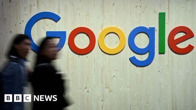 People walk in front of a Google logo.