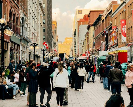 A scene from Sparks Street in Ottawa, a pedestrian street with people walking around and heading into and out of shops.