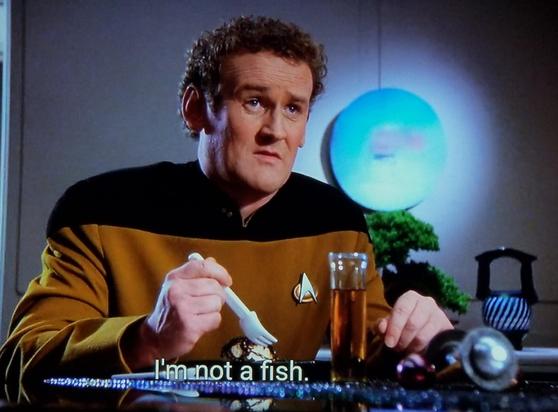 Star Trek The Next Generation scene. We're in "personal quarters" with chief Miles O'Brien, who's never once been told by McDonald's that the ice cream machine is broken. He's sitting at the dinner table and holding a spork type future space utensil.  O'Brien, who can lead a horse to water and also make it drink, is looking kind of squeemish and is speaking to someone across the table. Closed caption reads, "I'm not a fish."