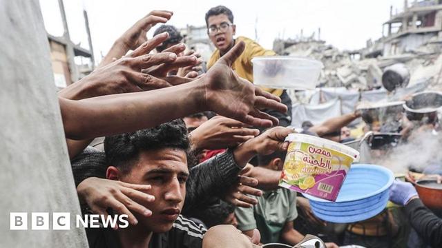 Displaced Palestinians hold out pans at a community kitchen in Jabalia refugee camp, northern Gaza (24 April 2025)