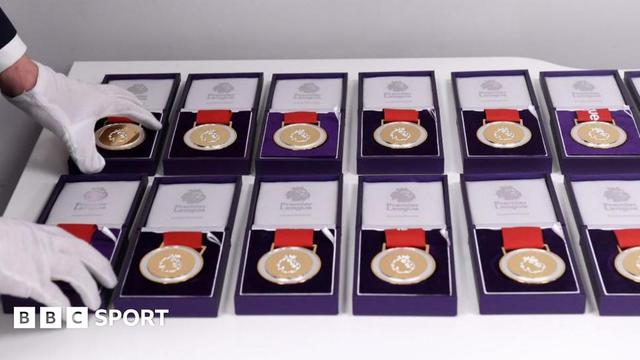 A set of 12 Premier League winners medals sits in cushioned purple display cases while a man wearing white gloves arranges them neatly