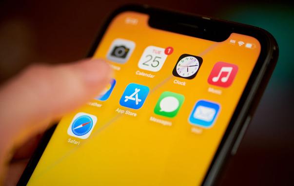 Thumb hovering over the Apple App Store icon on an iPhone with an orange backgbround.
