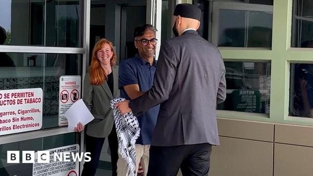 Badar Khan Suri smiling while meeting a man holding a keffiyeh, with a woman standing behind him