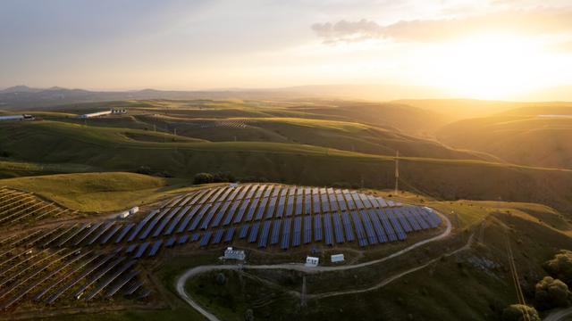 A view of a hlltop lit by the rising sun, with solar panels covering it.
