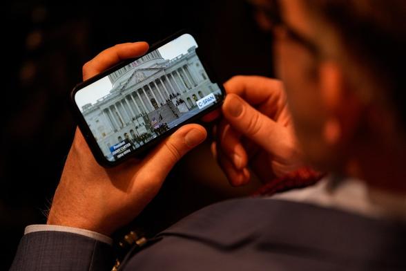 An attendee of a Capitol Rotunda memorial service for Jimmy Carter watches the C-SPAN feed of the scene as the late president's casket arrives at the Capitol.