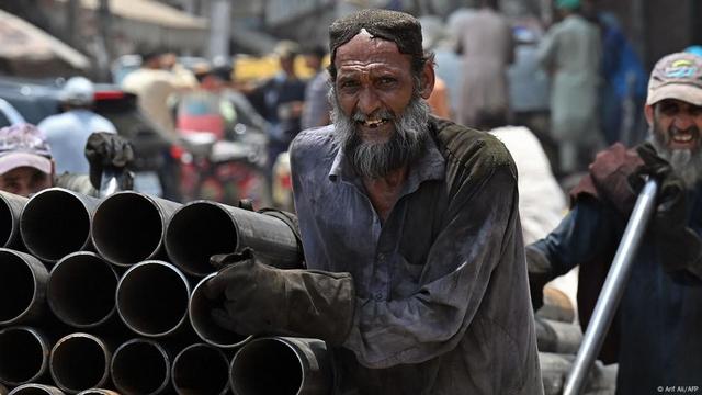 Laborers push a cart along a road on a hot day in Lahore, Pakistan.