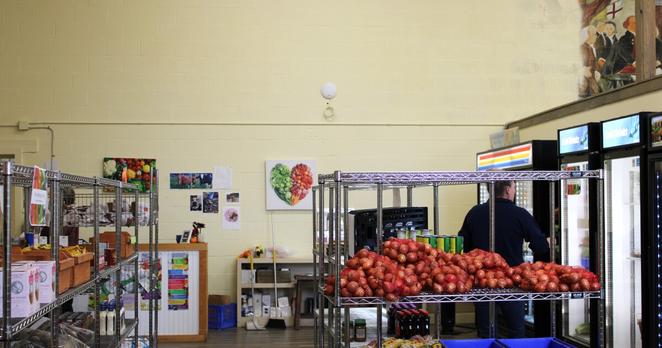 A person reaches into a fridge. Metal shelves hold produce and other food items.